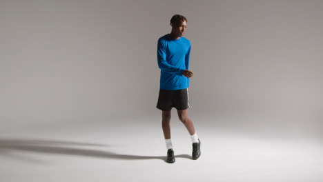 Studio-Shot-Of-Young-Male-Footballer-Warming-Up-With-Exercises-Before-Game