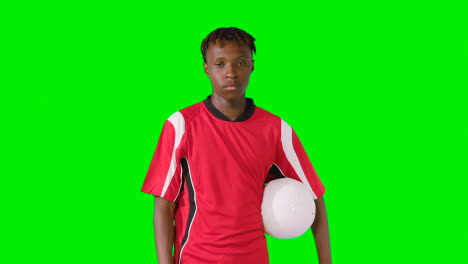 Studioporträt-Eines-Männlichen-Fußballers,-Der-Club-Kit-Mit-Ball-Unter-Dem-Arm-Vor-Grünem-Bildschirm-Trägt