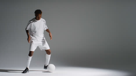 Studio-Shot-Of-Male-Footballer-Wearing-Club-Kit-Dribbling-With-Ball-