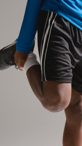 Vertical-Video-Studio-Shot-Of-Male-Footballer-Warming-Up-With-Exercises-Before-Game-