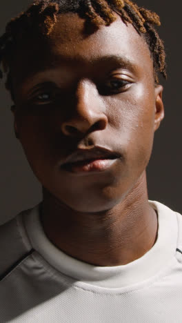 Vertical-Video-Studio-Portrait-Of-Young-Male-Footballer-Or-Sportsperson-Putting-On-Club-Kit-Shirt