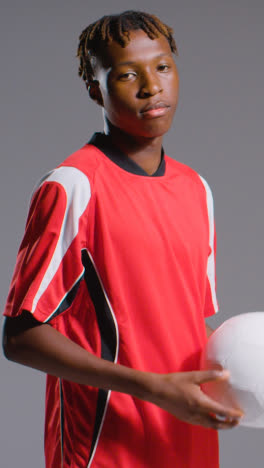 Vertical-Video-Studio-Portrait-Of-Young-Male-Footballer-Wearing-Club-Kit-With-Ball-Under-Arm-3