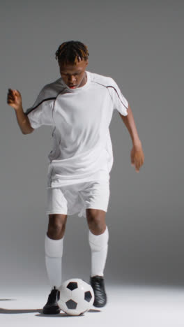 Vertical-Video-Close-Up-Studio-Shot-Of-Male-Footballer-In-Studio-Playing-Keepy-Uppy-Kicking-Ball-2