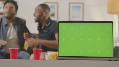 Two-Men-Celebrating-Watching-Sports-Game-On-TV-At-Home-With-Green-Screen-Laptop-In-Foreground-1