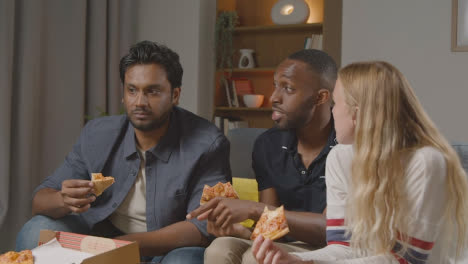 Multi-Cultural-Friends-Sitting-On-Sofa-At-Home-Watching-TV-Eating-Takeaway-Pizza-Delivery-3