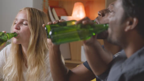 Multi-Cultural-Friends-Sitting-On-Sofa-At-Home-Talking-And-Drinking-Beer