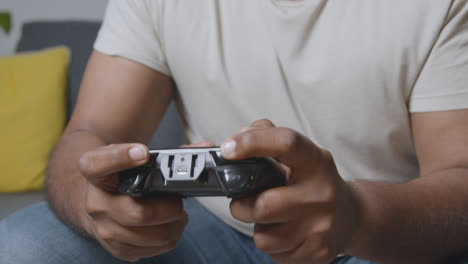 Close-Up-Of-Man-Holding-Controller-Sitting-On-Sofa-At-Home-Gaming-Online-1