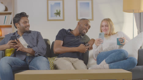 Multi-Cultural-Friends-Sitting-On-Sofa-At-Home-Together-All-Looking-At-Their-Mobile-Phones