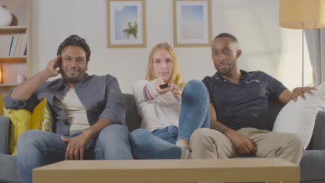 Woman-Telling-Male-Friends-To-Be-Quiet-As-They-Sit-On-Sofa-At-Home-Together-To-Watch-TV