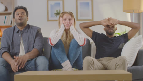 Disappointed-Multi-Cultural-Friends-Watching-Sports-Game-On-TV-Sitting-On-Sofa-At-Home-Together-2