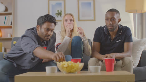 Multi-Cultural-Friends-Sitting-On-Sofa-At-Home-Together-Eating-Chips-And-Dips-Whilst-Watching-TV-2