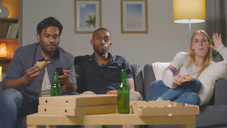 Multi-Cultural-Friends-Sitting-On-Sofa-At-Home-Watching-TV-Eating-Takeaway-Pizza-Delivery-4