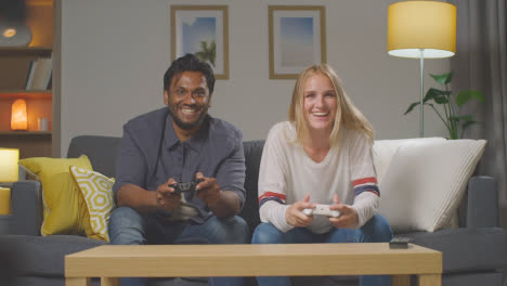 Multi-Cultural-Friends-Or-Couple-Sitting-On-Sofa-At-Home-Gaming-Online-4