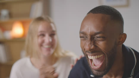 Couple-Or-Friends-Celebrating-Watching-Sports-Game-On-TV-Sitting-On-Sofa-At-Home-Drinking-Beer-Together