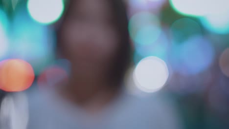 Coming-to-Focus-Portrait-of-the-Beautiful-Alternative-East-Asian-Girl-Smiling-on-Camera.-In-the-Background-Blurred-Big-City-Lights-Glowing.