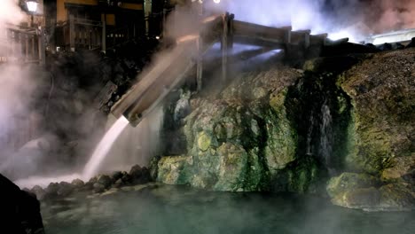 Kusatsu-Onsen,-una-terapia-termal-famosa-recurre-en-la-Prefectura-de-Gunma,-flujo-rápido-de-agua-en-la-pista-de-madera-en-la-noche-en-Japón.