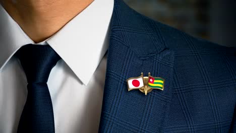 Businessman-Walking-Towards-Camera-With-Friend-Country-Flags-Pin-Japan---Togo