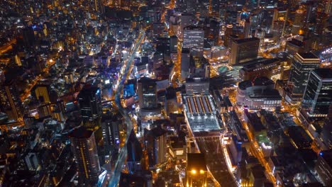 Aerial-night-hyper-lapse-over-Osaka-city-Japan-with-Umeda(Osaka)-train-station-and-many-skyscraper-building-and-vehicles-transporting-along-the-road.