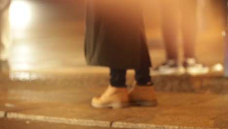 Person-standing-by-city-street-at-night.-Girl-wearing-boots-stands-seen-through-window-in-4K