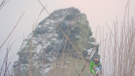 Snowboarder-senderismo-junto-a-grandes-montañas-rocosas-en-el-clima-nevado