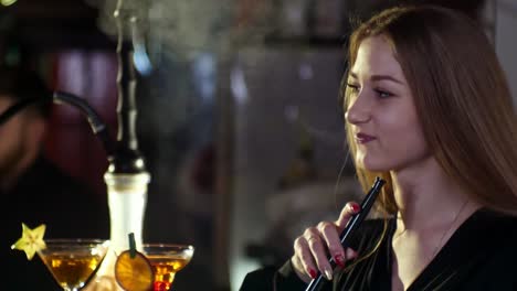 Mädchen-in-einer-Bar-am-Abend,-eine-Shisha-rauchen,-Cocktails-trinken-und-sprechen-miteinander-in-Zeitlupe-in-4-k-Auflösung