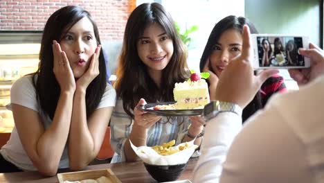 Friends-group-of-Asian-people,-one-male-taking-photos-of-three-female-friends-with-a-strawberry-cake-at-restaurant-while-girls-keep-changing-poses