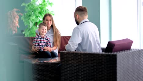 Mother-keeping-on-her-knees-little-son-sitting-in-chair-talking-with-doctor