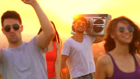 La-gente-feliz-con-una-caja-de-auge-bailando-sobre-un-fondo-de-sol.-cámara-lenta