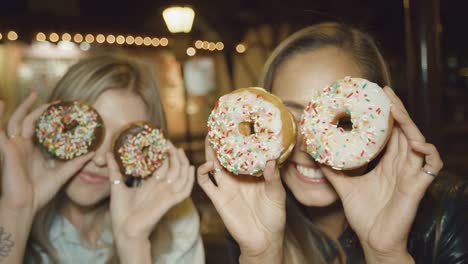 Porträt-von-zwei-süßen-Mädchen,-die-Spaß-macht-lustige-Gesichter-mit-Donuts-über-Augen