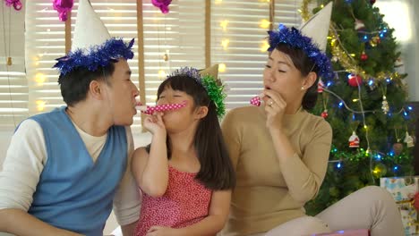 Best-time-together.-Happy-young-family-sitting-on-the-bed-and-blowing-party-horn-blowers-while-all-of-them-wearing-party-hats-in-Slow-motion.
