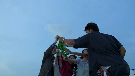 Group-of-young-friends-dancing-and-having-fun-celebrate-with-toast-and-clinking-raising-glasses-at-summer-rooftop-party.-Slow-Motion.