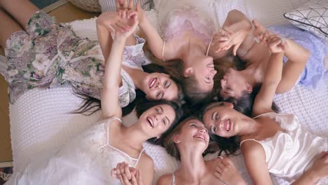 hen-party,-top-view-on-сheerful-female-models-in-sexy-pajamas-lie-on-bed-and-have-fun-into-camera-at-bedroom