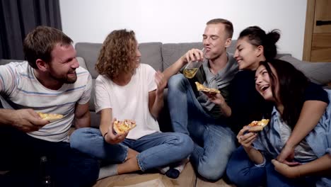 Freundschaft,-Essen,-inländische-Partyzeit---Pizza-bestellen-fröhlich-kaukasischen-Freunde,-Spaß,-auf-Boden-drinnen-sitzen-und-lachen,-Essen,-trinken.-Vorderansicht