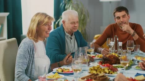 Familiares-y-amigos-en-la-mesa-del-comedor.-Senior-pareja-hablando,-bromeando-y-comer.-Viejas-y-jóvenes-personas-riendo-divertido.