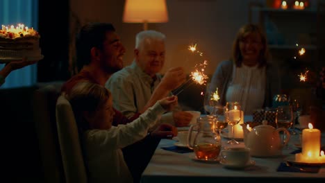 Following-Shot-of-a-Daughter-Bringing-Birtday-Cake-with-Candlelights-to-Her-Senior-Mother.-Family-Dinner-and-Celebration,-People-Gathered-at-the-Evening-Dinner-Table.