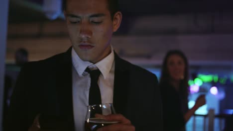 Well-dressed-young-man-in-a-nightclub-holding-a-drink-and-texting