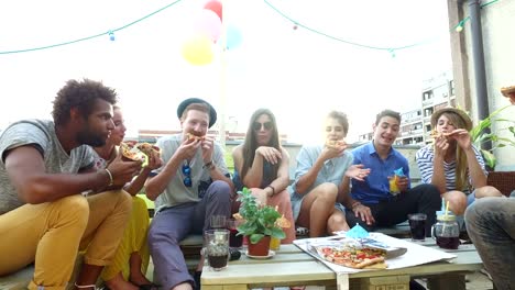 Junge-Menschen-rund-um-den-Tisch-sitzen-und-Essen-Pizza-auf-der-Dachterrasse