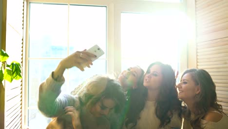vier-schöne-Mädchen-schießen-Selfie-am-Fenster-sitzen.-Freundinnen-Spaß-haben-und-Lachen-im-Schlafzimmer
