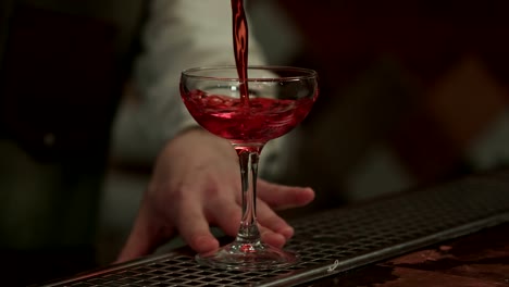 Barman-vertiendo-alcohol-rojo-preparando-cosmopolita-en-Copa-de-champán