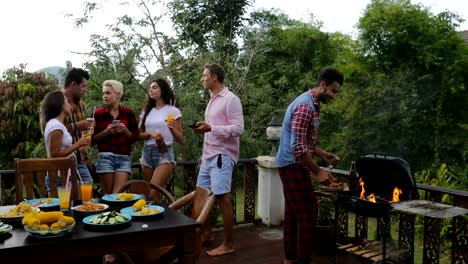 Junge-Leute-reden-mit-Zelle-Smartphones-während-Latein-Mann-Kochen-Barbecue-Freundesgruppe-treffen-auf-die-Sommerterrasse-Kommunikation