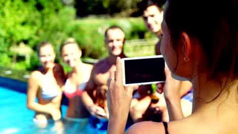 Lächelnde-Frau-Klick-Fotos-von-Freunden-von-Handy-nahe-am-Pool