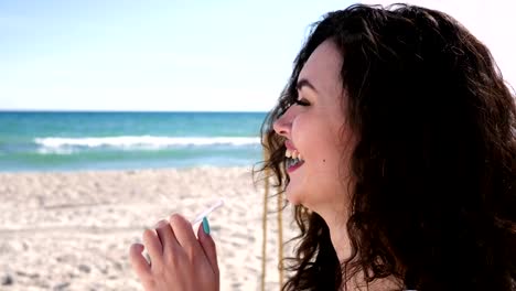 Retrato-de-mujer-feliz-con-el-cabello-rizado-en-la-playa,-Hola-gesto-femenino,-mujer-bebidas-cóctel-a-través-de-la-paja-y-el-resto,-temporada-de-verano