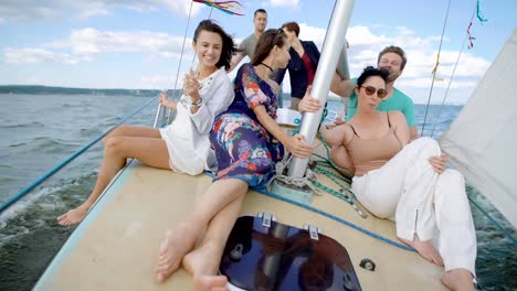 A-company-of-friends-ride-on-a-yacht-on-the-high-seas-or-the-ocean,-buddies-sit-on-deck-and-enjoy-a-light-wind-that-blows-their-hair-and-clothes