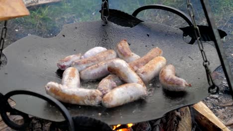 Flipped-Tasty-Juicy-Sausages-Fry-In-a-Frying-Pan-Suspended-Over-Fire,-Barbecue