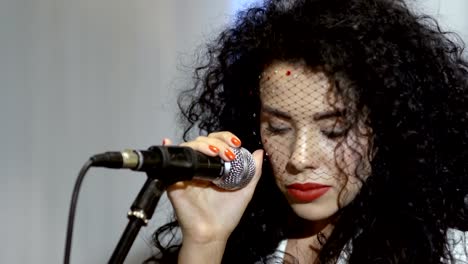 Beautiful-curly-brunette-with-veil-on-face-sings-in-microphone