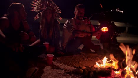 Young-rebel-motorcyclist-friends-drinking-and-smoking-around-campfire