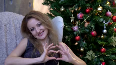 Pretty-young-girl-making-a-heart-with-her-hands-on-christmas-tree-background