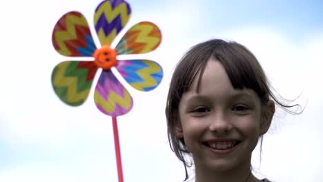 hermosa-chica-con-juguete-de-molino-de-viento-en-la-naturaleza-sonriente-y-mirando-a-la-cámara