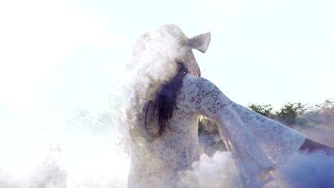 On-a-sunny-day,-a-woman-walks-across-the-field-with-a-colored-smoke-flare-in-a-white-dress-against-a-nature-background.-Concept-life-style,-ecology,-colorful-happy-people-freedom-wonderfully-beautiful