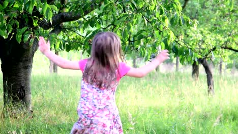 Eine-niedliche-Mädchen-tanzt-in-den-Naturgarten.-Kleine-Mädchen-tanzt-und-springt-auf-einem-kleinen-Trampolin.-Kleines-Mädchen-trägt-geblümten-Kleid-und-weißen-Hut